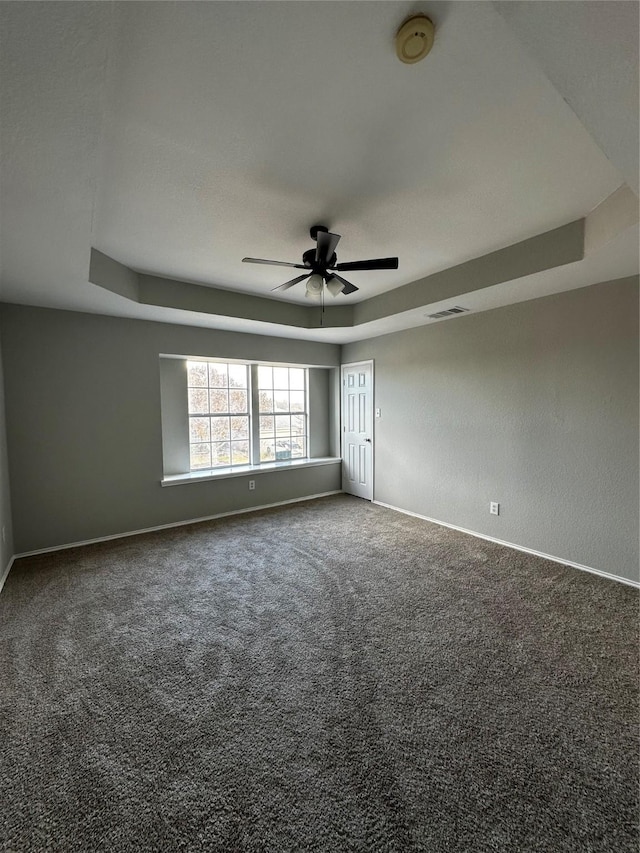 carpeted spare room with ceiling fan and a raised ceiling