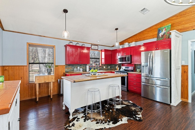 kitchen featuring butcher block countertops, appliances with stainless steel finishes, dark wood-type flooring, vaulted ceiling, and a kitchen island