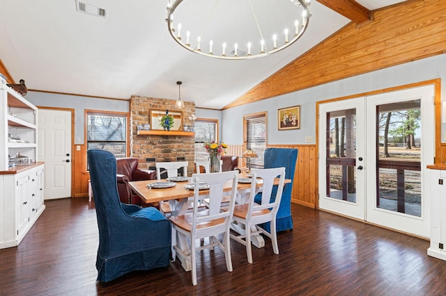 dining area with dark wood-type flooring, a stone fireplace, french doors, vaulted ceiling with beams, and a notable chandelier