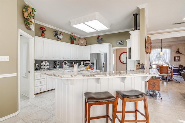 kitchen with white cabinetry, stainless steel fridge, light tile patterned flooring, light stone countertops, and crown molding