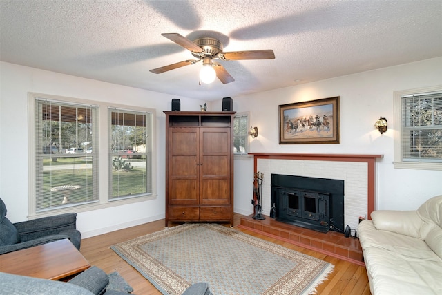 living room featuring a textured ceiling, ceiling fan, a tile fireplace, and light wood-type flooring