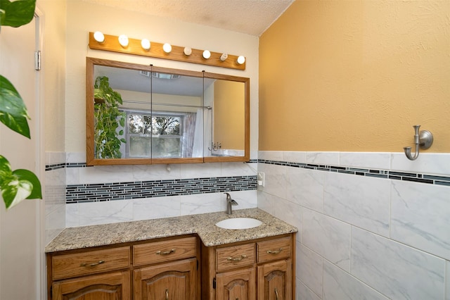 bathroom with a textured ceiling, vanity, and tile walls