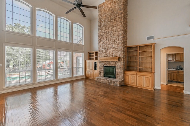 unfurnished living room featuring ceiling fan, dark wood-type flooring, a stone fireplace, and a towering ceiling