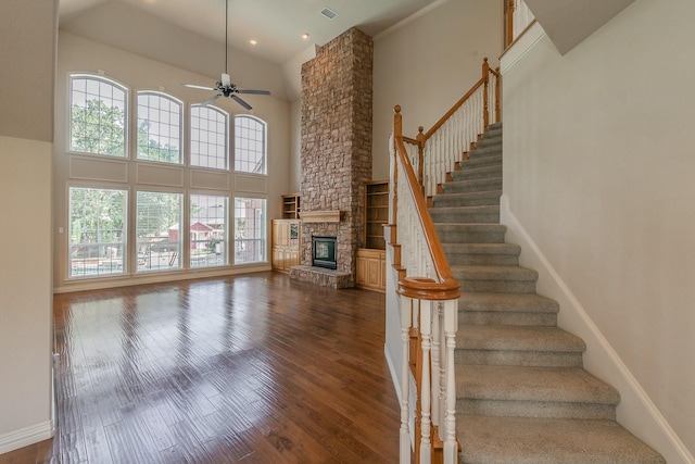 staircase with ceiling fan, a healthy amount of sunlight, a fireplace, and a high ceiling