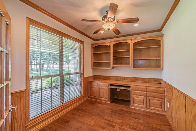 unfurnished office featuring crown molding, built in desk, dark hardwood / wood-style floors, and ceiling fan