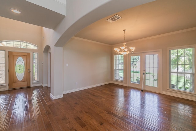 foyer entrance featuring a wealth of natural light, dark hardwood / wood-style floors, ornamental molding, and a notable chandelier