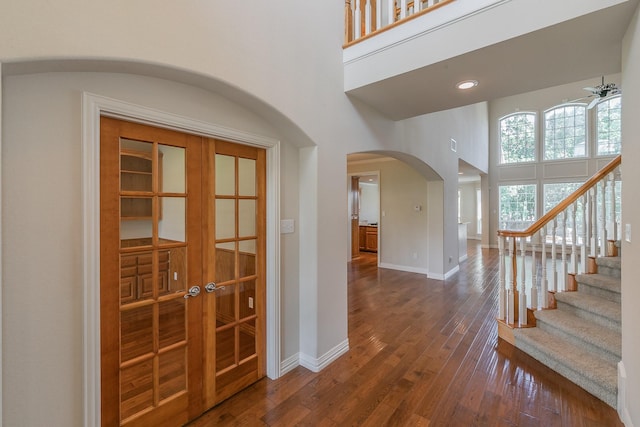 foyer with dark wood-type flooring, ceiling fan, and a towering ceiling