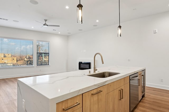 kitchen featuring light stone counters, sink, pendant lighting, and a center island with sink