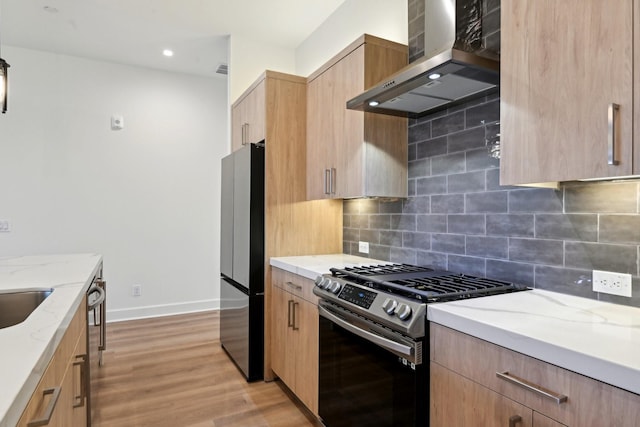 kitchen featuring appliances with stainless steel finishes, decorative backsplash, light wood-type flooring, wall chimney range hood, and light stone counters