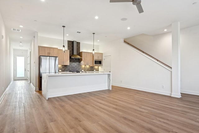 kitchen with pendant lighting, wall chimney exhaust hood, stainless steel appliances, light hardwood / wood-style floors, and backsplash