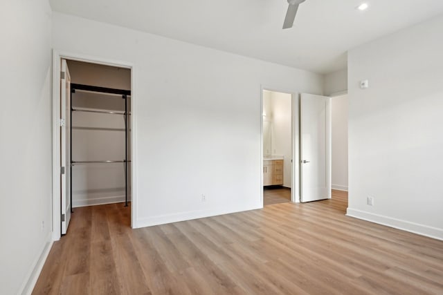 unfurnished bedroom featuring a walk in closet, connected bathroom, a closet, ceiling fan, and light hardwood / wood-style flooring