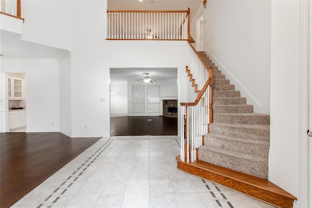 entrance foyer with ceiling fan, a fireplace, a towering ceiling, light tile patterned flooring, and ornamental molding