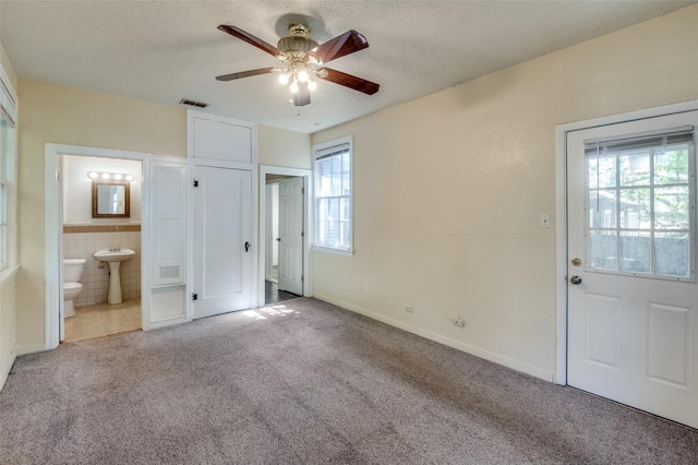 unfurnished bedroom featuring a textured ceiling, ceiling fan, ensuite bathroom, and light colored carpet