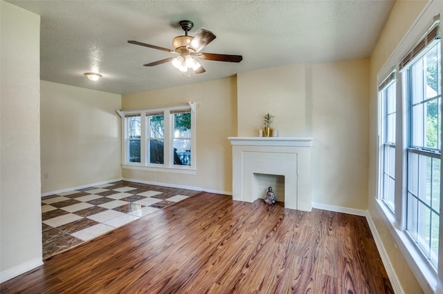 unfurnished living room featuring ceiling fan, plenty of natural light, wood-type flooring, and a textured ceiling