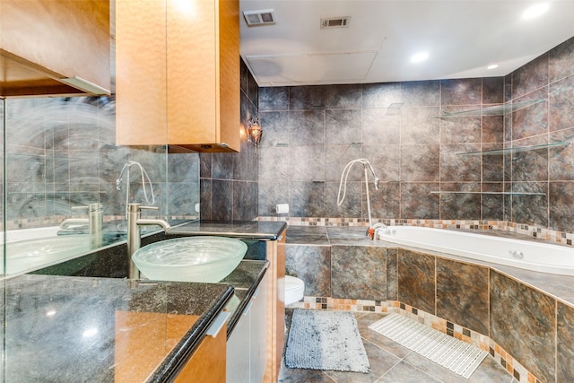 bathroom featuring tiled bath, toilet, vanity, and tile patterned flooring