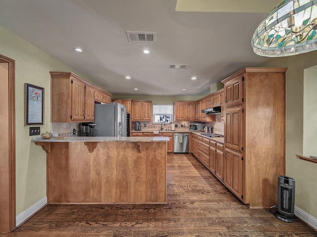 kitchen with appliances with stainless steel finishes, dark hardwood / wood-style flooring, decorative backsplash, kitchen peninsula, and a breakfast bar area