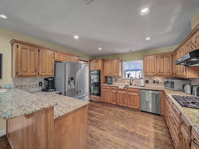 kitchen featuring hardwood / wood-style floors, kitchen peninsula, decorative backsplash, stainless steel appliances, and ventilation hood