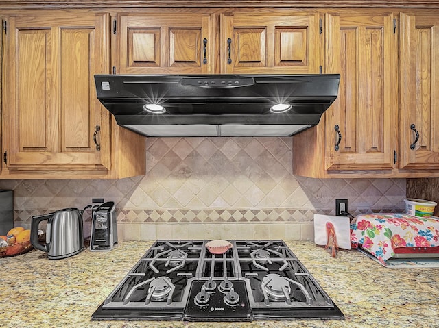 kitchen featuring range hood, decorative backsplash, black gas stovetop, and light stone countertops