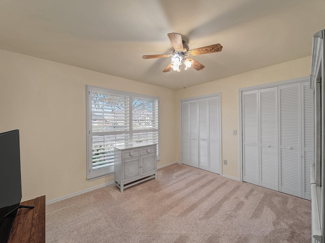 unfurnished bedroom featuring ceiling fan, light carpet, and multiple closets