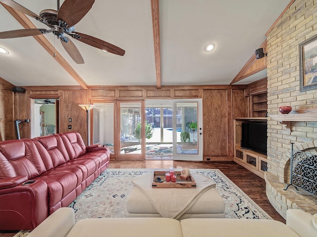 living room with wooden walls, a brick fireplace, ceiling fan, dark hardwood / wood-style flooring, and lofted ceiling with beams