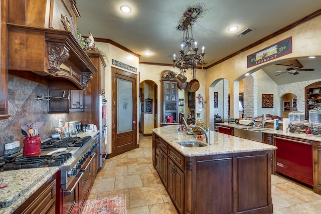 kitchen featuring an island with sink, appliances with stainless steel finishes, light stone countertops, ceiling fan with notable chandelier, and sink