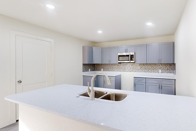 kitchen with gray cabinetry, decorative backsplash, light hardwood / wood-style floors, and sink