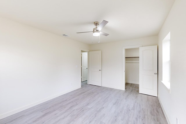 unfurnished bedroom featuring ceiling fan, a walk in closet, a closet, and light hardwood / wood-style floors