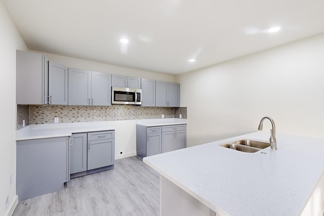 kitchen featuring backsplash, gray cabinets, kitchen peninsula, sink, and light hardwood / wood-style flooring