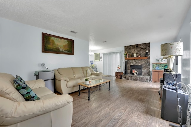 living room featuring a stone fireplace, a textured ceiling, and light hardwood / wood-style floors