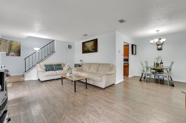 living room with light hardwood / wood-style floors, a textured ceiling, and an inviting chandelier