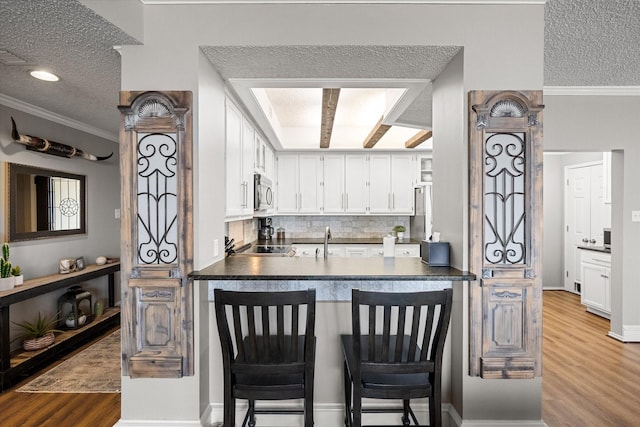 kitchen featuring a textured ceiling, white cabinetry, tasteful backsplash, hardwood / wood-style flooring, and crown molding