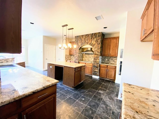 kitchen featuring backsplash, a center island, pendant lighting, light stone counters, and sink