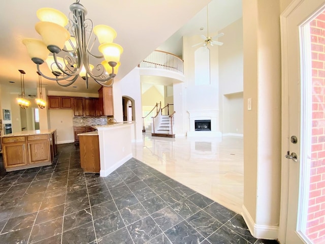 kitchen featuring kitchen peninsula, decorative backsplash, a high ceiling, hanging light fixtures, and ceiling fan with notable chandelier