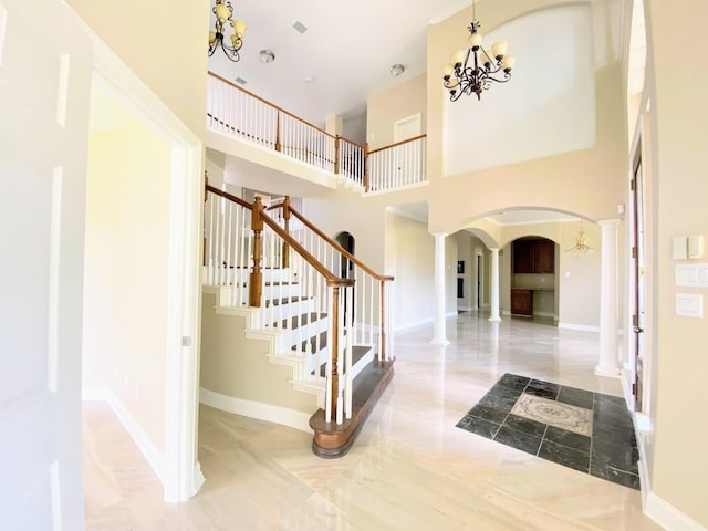 stairway with a towering ceiling, a notable chandelier, and ornate columns