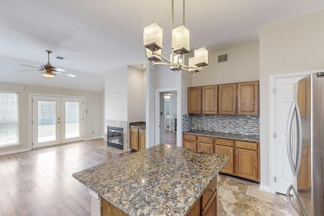 kitchen with tasteful backsplash, a center island, hanging light fixtures, stainless steel fridge, and ceiling fan