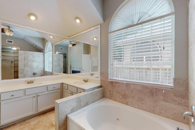 bathroom with a fireplace, vanity, tiled bath, and vaulted ceiling