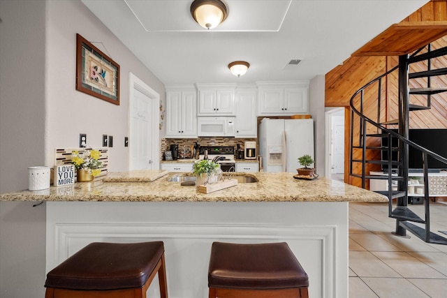 kitchen featuring white cabinets, kitchen peninsula, light stone counters, and white appliances