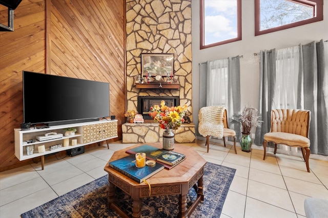 living room featuring a fireplace, light tile patterned floors, a towering ceiling, and wood walls