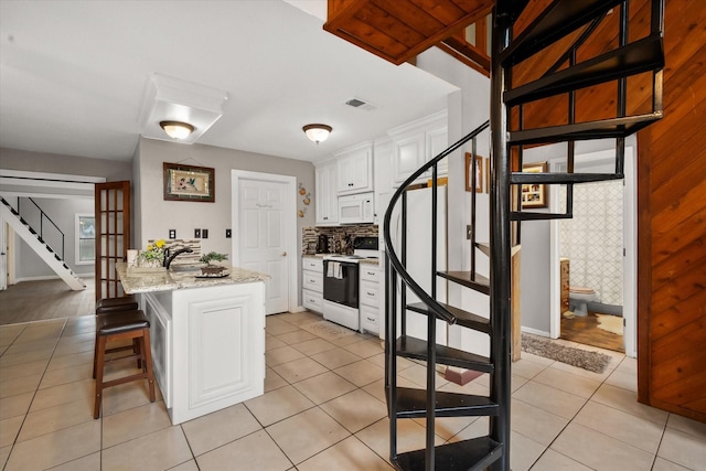 kitchen featuring tasteful backsplash, white appliances, a kitchen breakfast bar, light stone countertops, and white cabinets