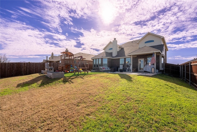 back house at dusk with a playground, a patio area, and a lawn