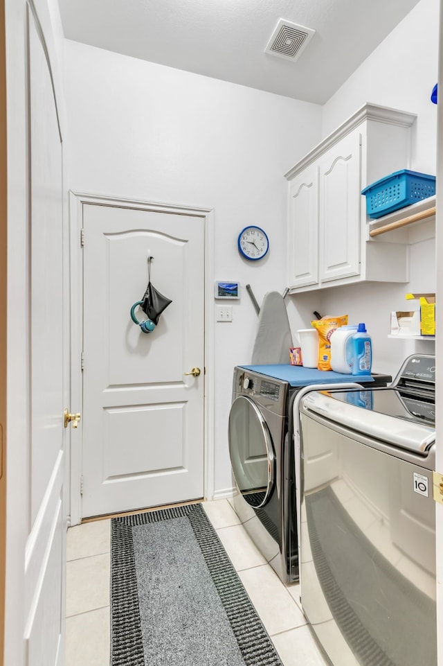 clothes washing area featuring light tile patterned floors, washing machine and dryer, and cabinets