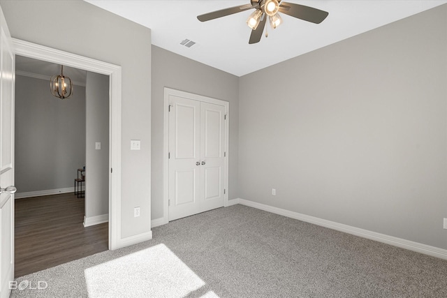 unfurnished bedroom featuring carpet, visible vents, baseboards, a closet, and ceiling fan with notable chandelier