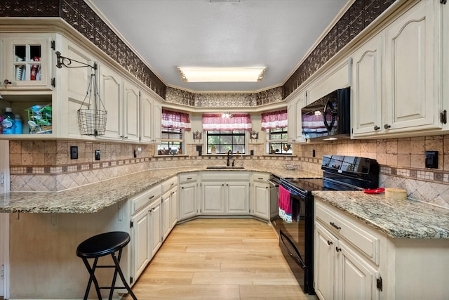 kitchen featuring sink, kitchen peninsula, light stone counters, and black appliances