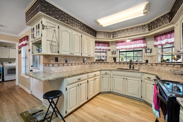 kitchen featuring washer / dryer, light stone counters, black electric range oven, crown molding, and a sink