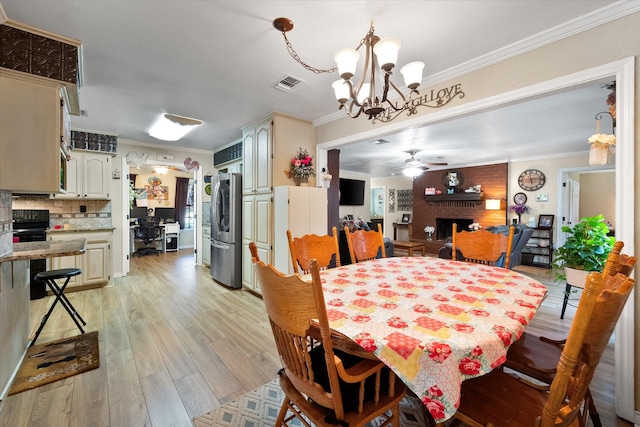 dining room featuring a fireplace, crown molding, visible vents, light wood-style floors, and ceiling fan with notable chandelier