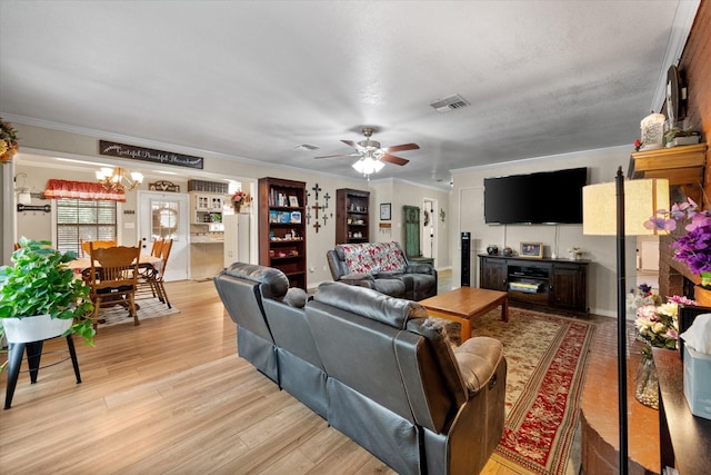 living room with light wood-type flooring, visible vents, ornamental molding, and ceiling fan with notable chandelier