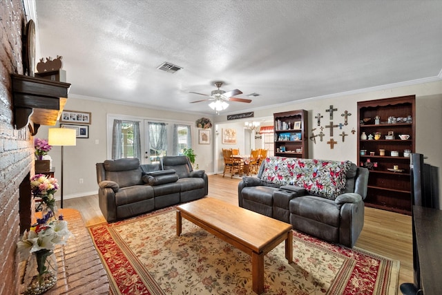 living room featuring visible vents, ornamental molding, light wood-style floors, a large fireplace, and a textured ceiling