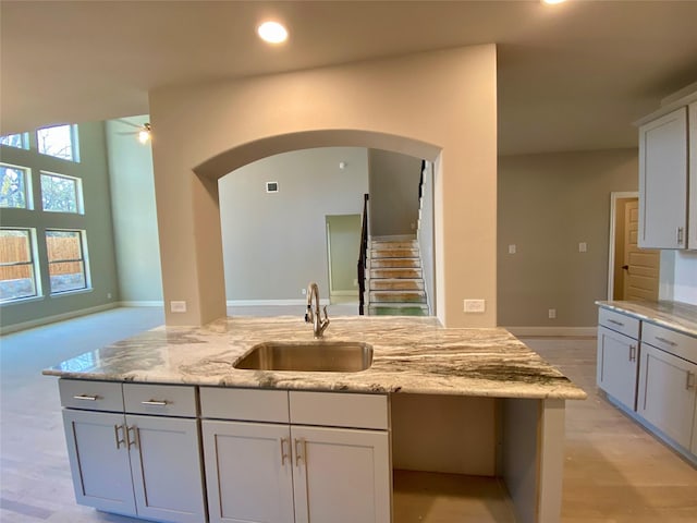 kitchen with light stone countertops, sink, light wood-type flooring, and a healthy amount of sunlight