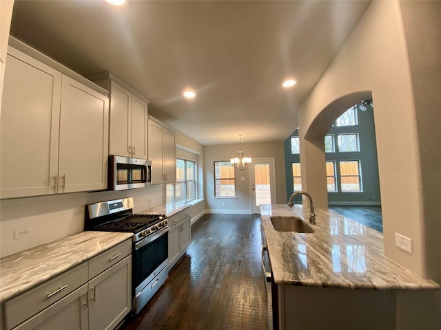 kitchen featuring a notable chandelier, a sink, appliances with stainless steel finishes, light stone countertops, and dark wood-style floors