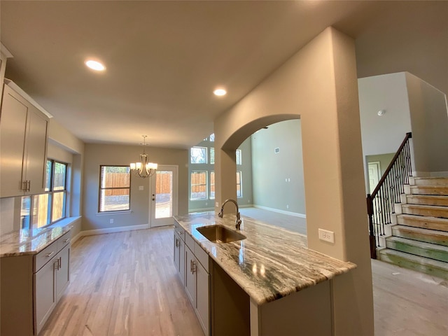 kitchen with decorative light fixtures, sink, a kitchen island with sink, plenty of natural light, and light stone counters